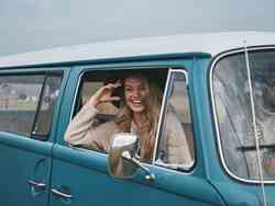Eine Frau lacht aus dem Fenster eines blauen VW-Bus.